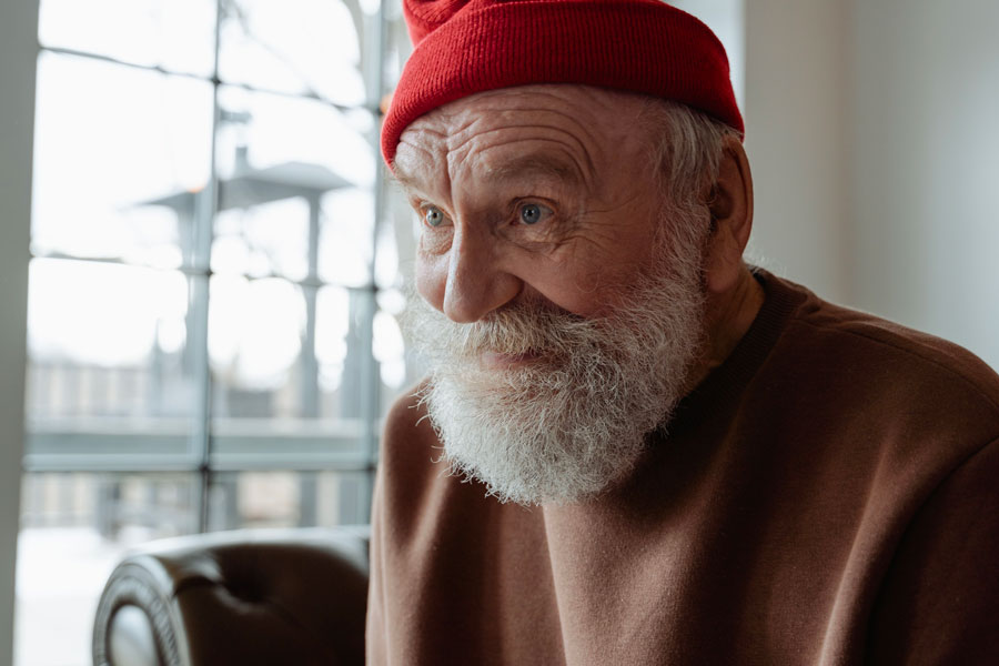 Homme âgé portant un bonnet rouge, chaudement habillé chez lui pendant l’hiver