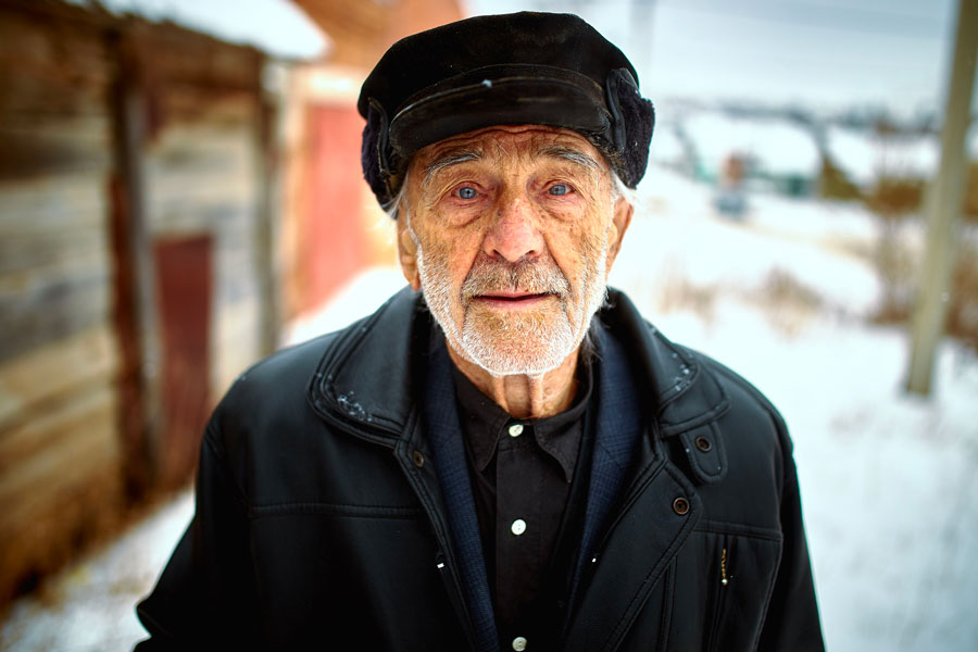 Homme âgé en manteau et casquette dans un village enneigé